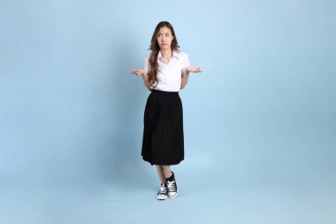 The young Asian student with uniform standing on the blue background.