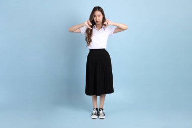 The young Asian student with uniform standing on the blue background.