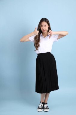 The young Asian student with uniform standing on the blue background.