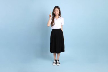 The young Asian student with uniform standing on the blue background.