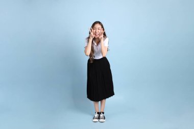 The young Asian student with uniform standing on the blue background.