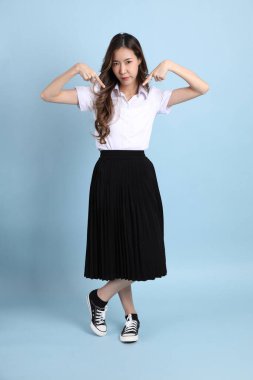 The young Asian student with uniform standing on the blue background.