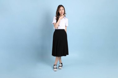 The young Asian student with uniform standing on the blue background.