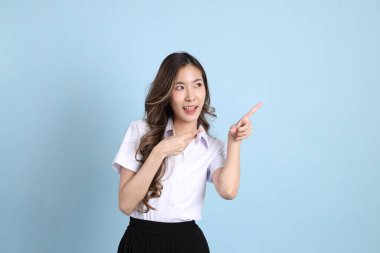The young Asian student with uniform standing on the blue background.