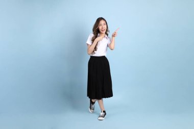 The young Asian student with uniform standing on the blue background.