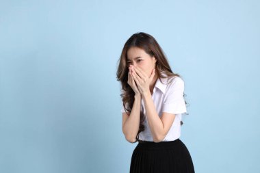 The young Asian student with uniform standing on the blue background.