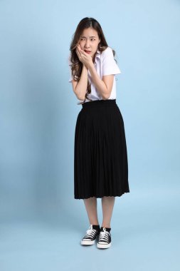 The young Asian student with uniform standing on the blue background.