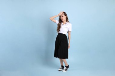 The young Asian student with uniform standing on the blue background.