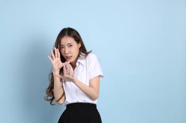 The young Asian student with uniform standing on the blue background.