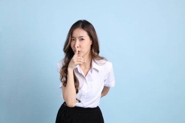 The young Asian student with uniform standing on the blue background.