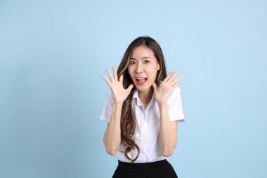 The young Asian student with uniform standing on the blue background.