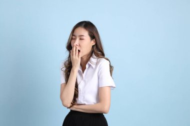 The young Asian student with uniform standing on the blue background.