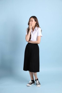 The young Asian student with uniform standing on the blue background.