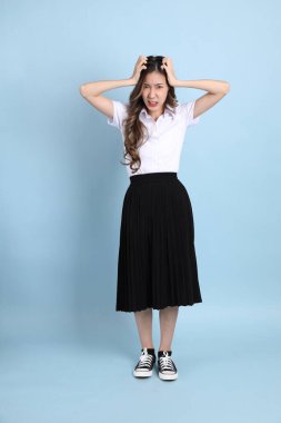 The young Asian student with uniform standing on the blue background.