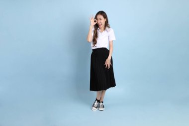 The young Asian student with uniform standing on the blue background.
