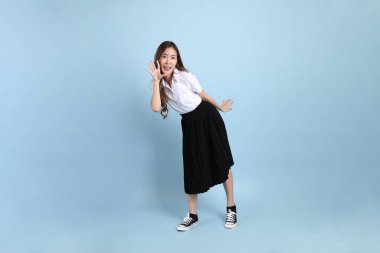 The young Asian student with uniform standing on the blue background.
