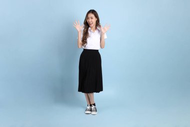The young Asian student with uniform standing on the blue background.