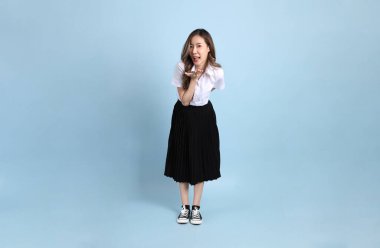 The young Asian student with uniform standing on the blue background.