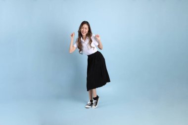 The young Asian student with uniform standing on the blue background.