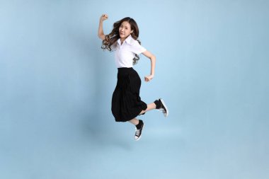 The young Asian student with uniform standing on the blue background.
