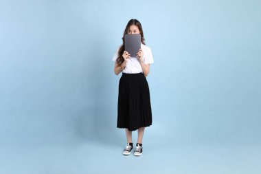The young Asian student with uniform standing on the blue background.