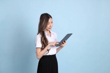 The young Asian student with uniform standing on the blue background.