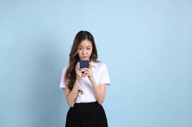 The young Asian student with uniform standing on the blue background.