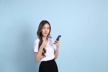 The young Asian student with uniform standing on the blue background.