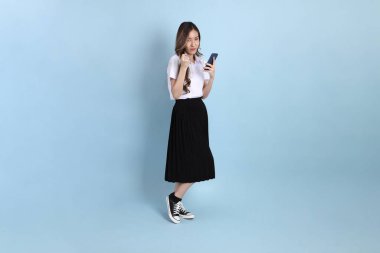 The young Asian student with uniform standing on the blue background.