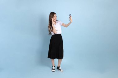 The young Asian student with uniform standing on the blue background.
