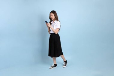 The young Asian student with uniform standing on the blue background.