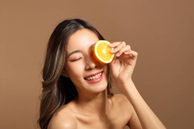 The beautiful  Asian woman showing skin with brown background holding lemon.