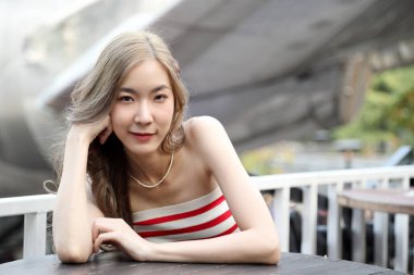 Yakışıklı Asyalı kadın açık hava restoranında poz verirken rahatlıyor..