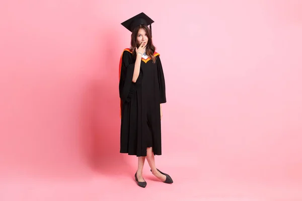 穿着毕业礼服站在粉色背景上的亚洲女人 — 图库照片