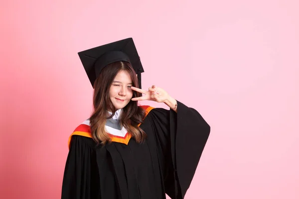 The Asian woman in graduation gown standing on the pink background.