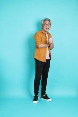 Yeşil arka planda duran sarı tişörtlü yakışıklı Asyalı adam..