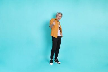 Yeşil arka planda duran sarı tişörtlü yakışıklı Asyalı adam..