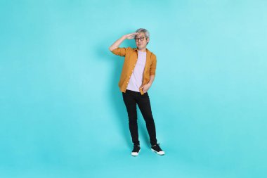 Yeşil arka planda duran sarı tişörtlü yakışıklı Asyalı adam..