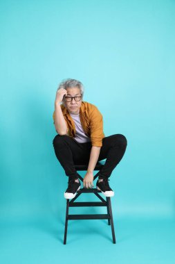 Yeşil arka planda oturan, sarı tişörtlü yakışıklı, kıdemli Asyalı adam..