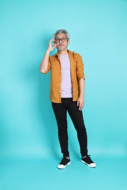 Yeşil arka planda duran sarı tişörtlü yakışıklı Asyalı adam..