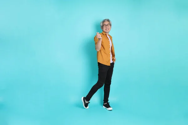 stock image The attractive senior Asian man with yellow shirt standing on the green background.