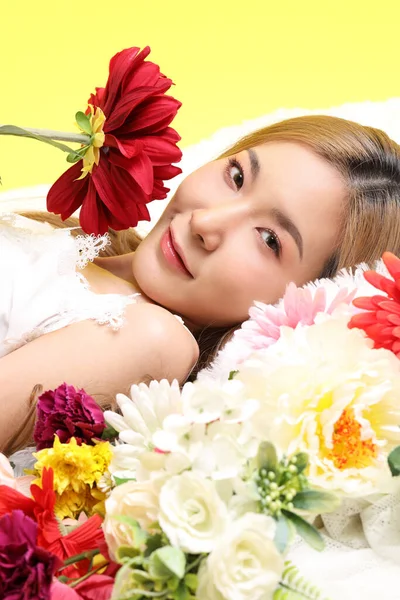 Sarı Arka Planda Çiçek Tarhında Uzanan Asyalı Güzel Kadın — Stok fotoğraf