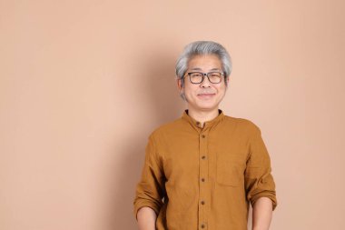 Kahverengi arka planda sarı gömlekli 40 'lı yaşlardaki Asyalı adam..