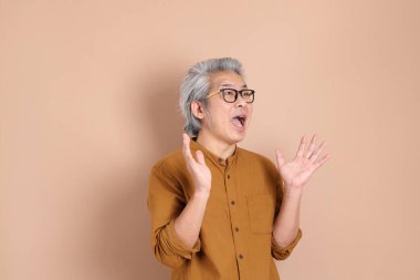 Kahverengi arka planda sarı gömlekli 40 'lı yaşlardaki Asyalı adam..