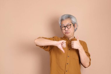 Kahverengi arka planda sarı gömlekli 40 'lı yaşlardaki Asyalı adam..