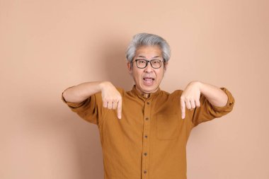 Kahverengi arka planda sarı gömlekli 40 'lı yaşlardaki Asyalı adam..