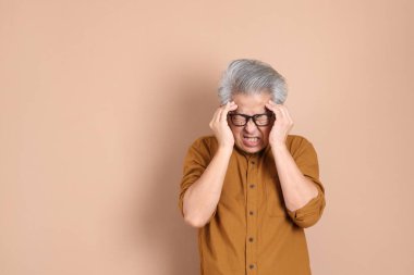 Kahverengi arka planda sarı gömlekli 40 'lı yaşlardaki Asyalı adam..