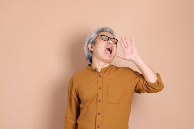 Kahverengi arka planda sarı gömlekli 40 'lı yaşlardaki Asyalı adam..