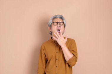 Kahverengi arka planda sarı gömlekli 40 'lı yaşlardaki Asyalı adam..