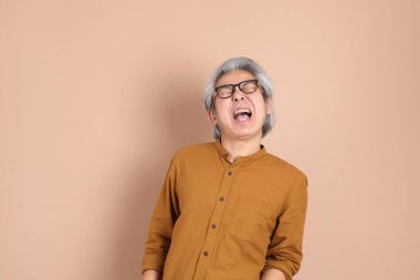 Kahverengi arka planda sarı gömlekli 40 'lı yaşlardaki Asyalı adam..